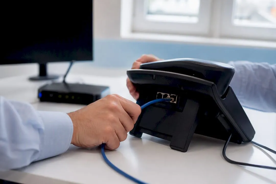 Hands connecting ethernet cable to VoIP phone